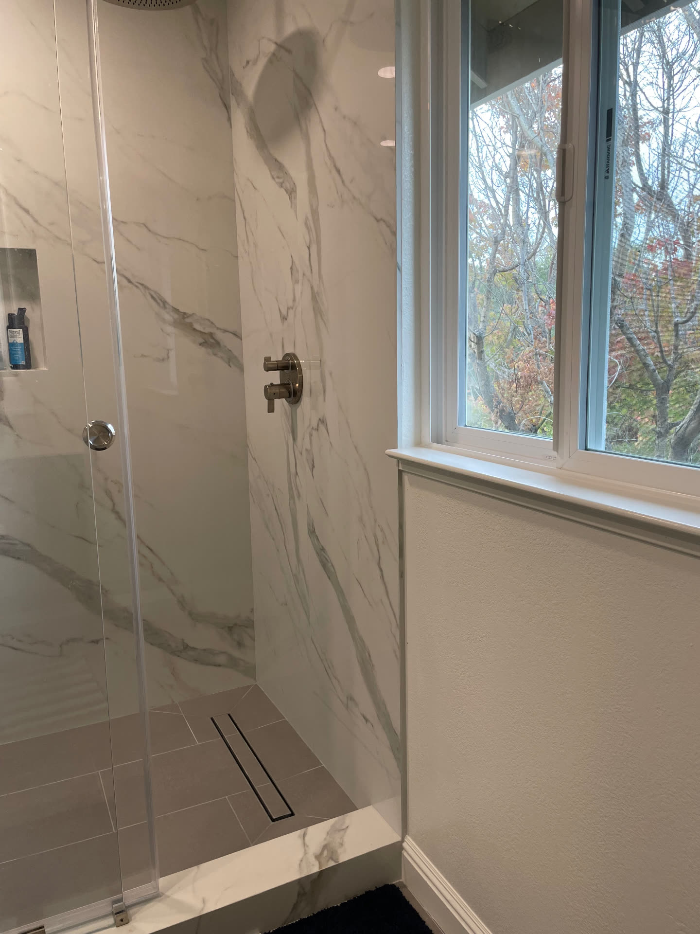 Shower interior with linear drain and brushed nickel valve beside a window