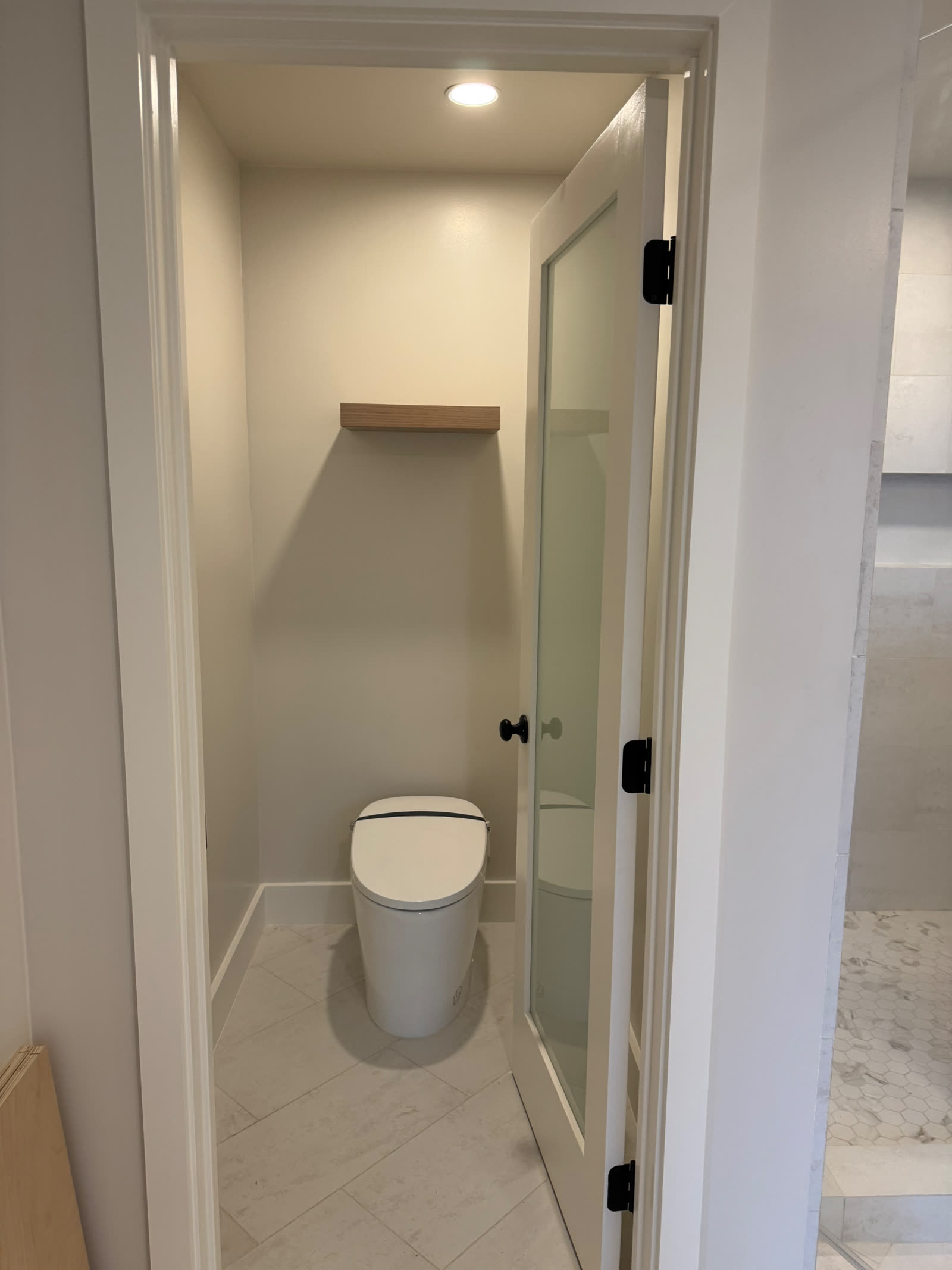 Private water closet with glass-panel door and floating oak shelf